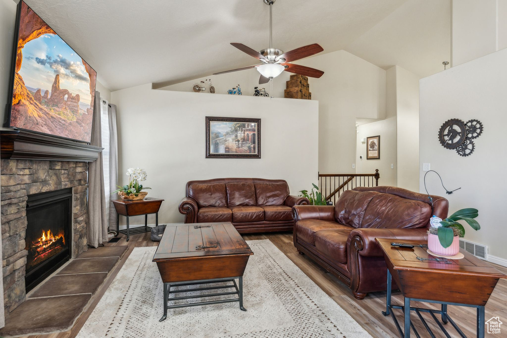 Living area featuring wood finished floors, a ceiling fan, a stone fireplace, and high vaulted ceiling