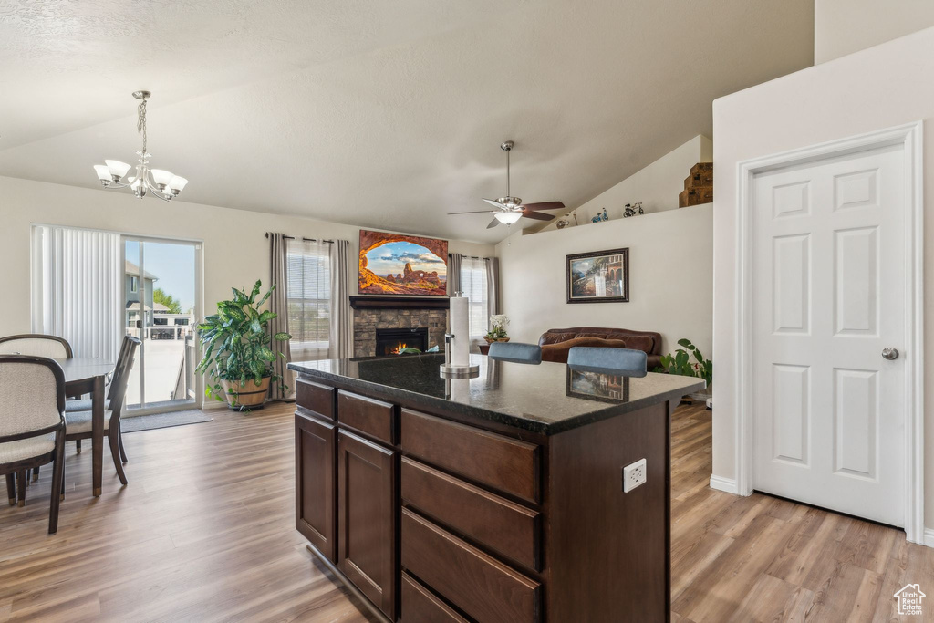Kitchen featuring vaulted ceiling, a ceiling fan, a chandelier, light wood-style floors, and a stone fireplace