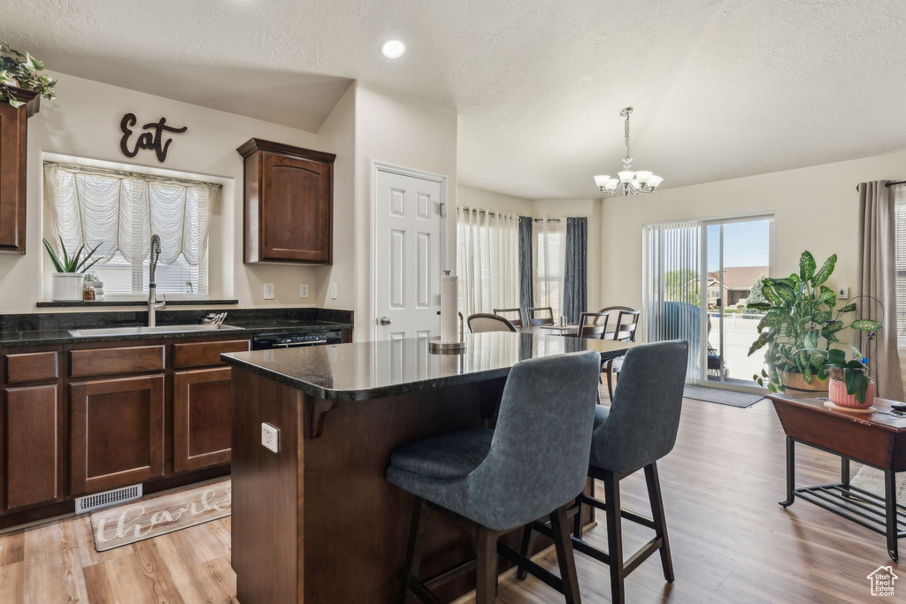 Kitchen featuring a breakfast bar area, a sink, dark countertops, a chandelier, and light wood finished floors
