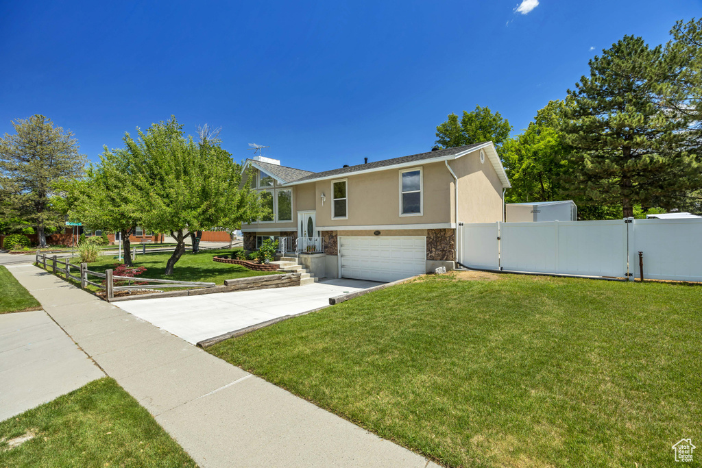 Raised ranch featuring stone siding, stucco siding, an attached garage, a gate, and driveway