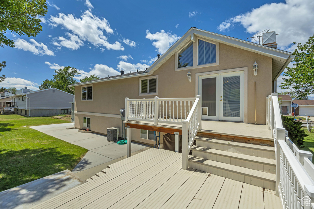 Back of property with stucco siding, a deck, a yard, and french doors