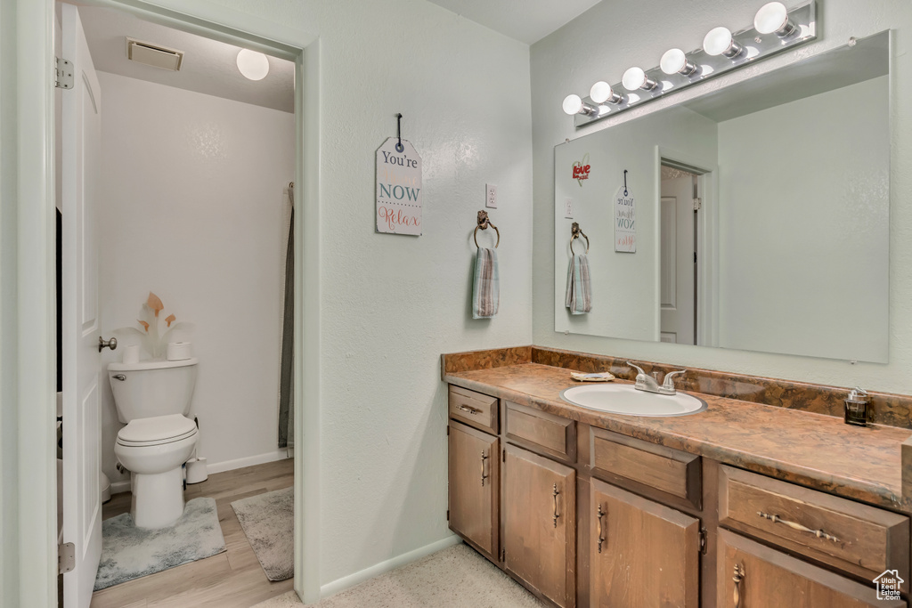 Full bath featuring vanity, toilet, baseboards, and wood finished floors