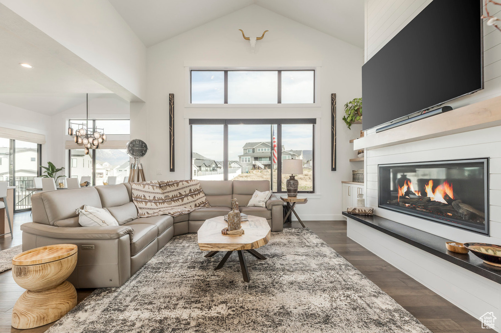 Living room featuring high vaulted ceiling, a glass covered fireplace, a chandelier, and dark wood-style flooring