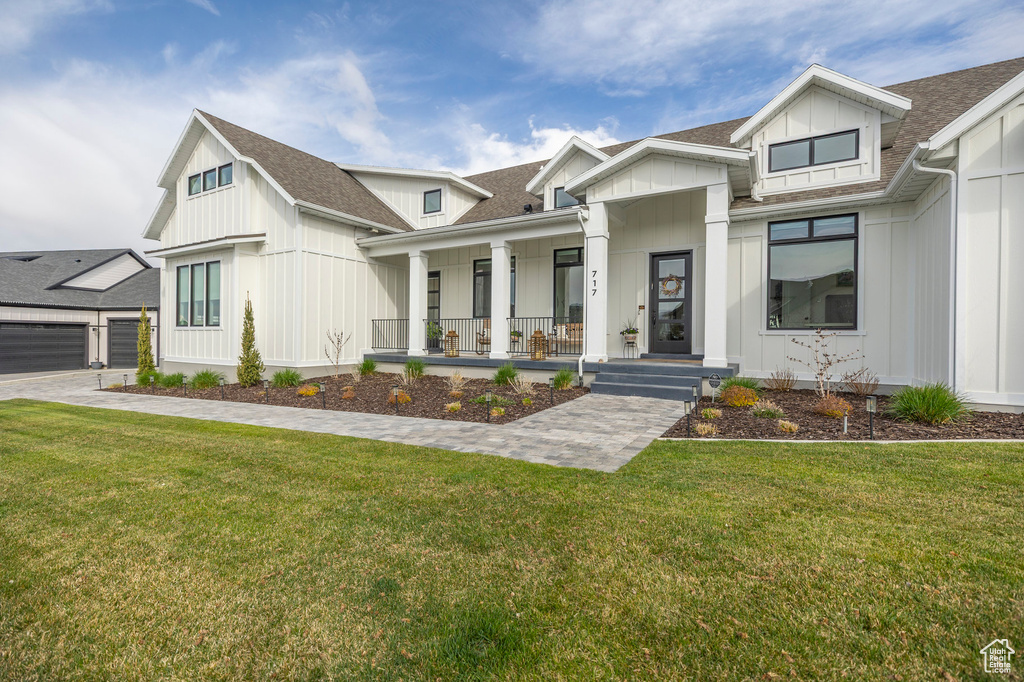 Modern farmhouse with a porch, board and batten siding, roof with shingles, and a front yard