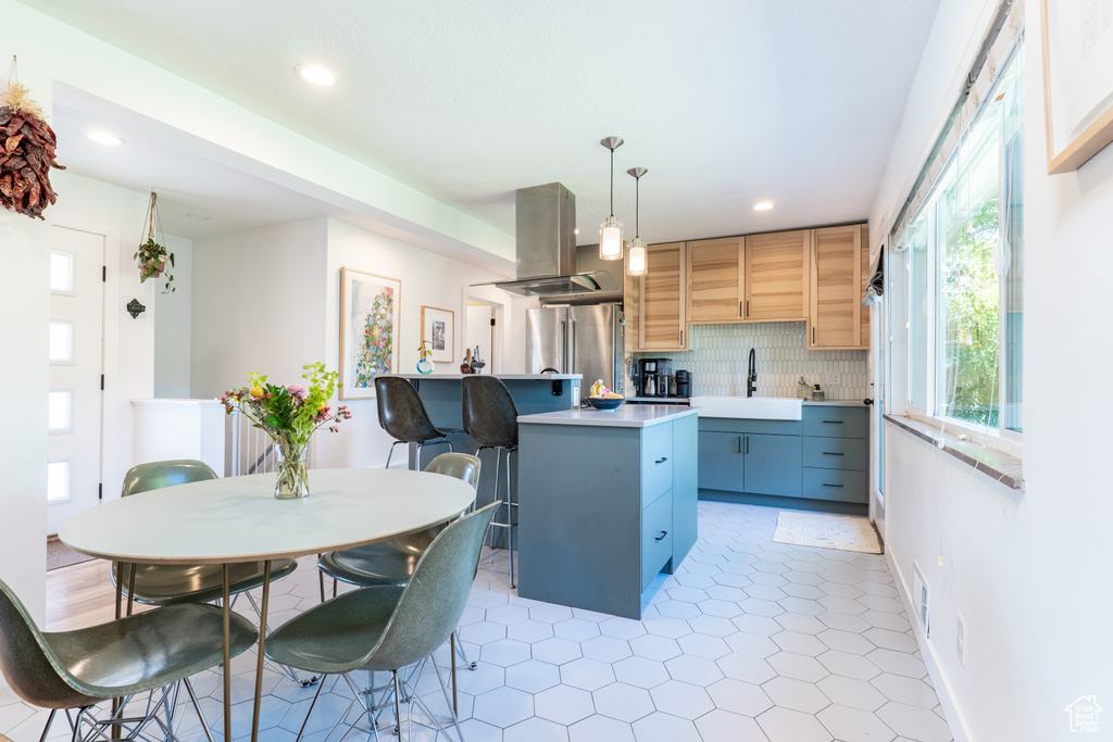 Kitchen featuring island exhaust hood, a sink, freestanding refrigerator, tasteful backsplash, and light countertops