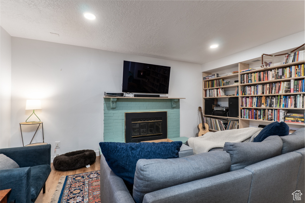 Living room with wood finished floors, a fireplace, a textured ceiling, recessed lighting, and baseboards