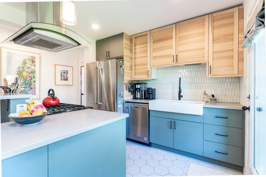 Kitchen with appliances with stainless steel finishes, a sink, range hood, decorative backsplash, and light countertops