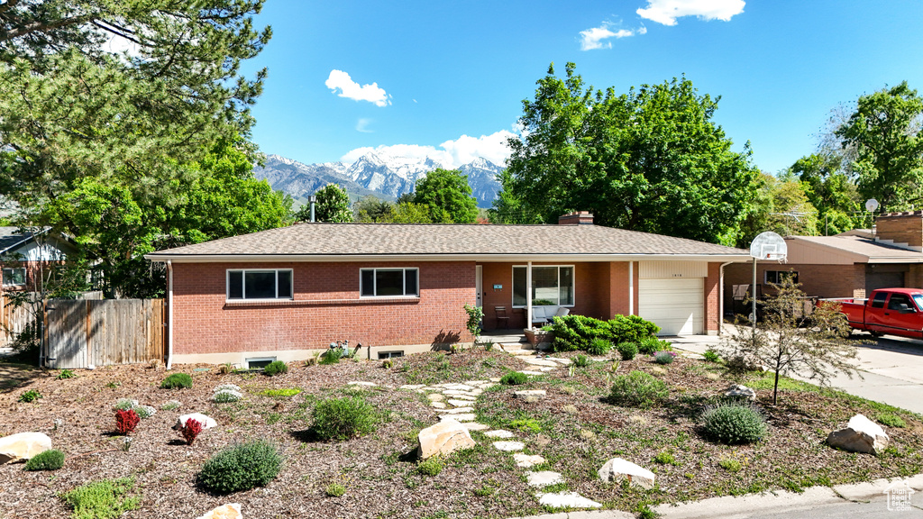 Single story home featuring a garage, brick siding, a mountain view, driveway, and a chimney