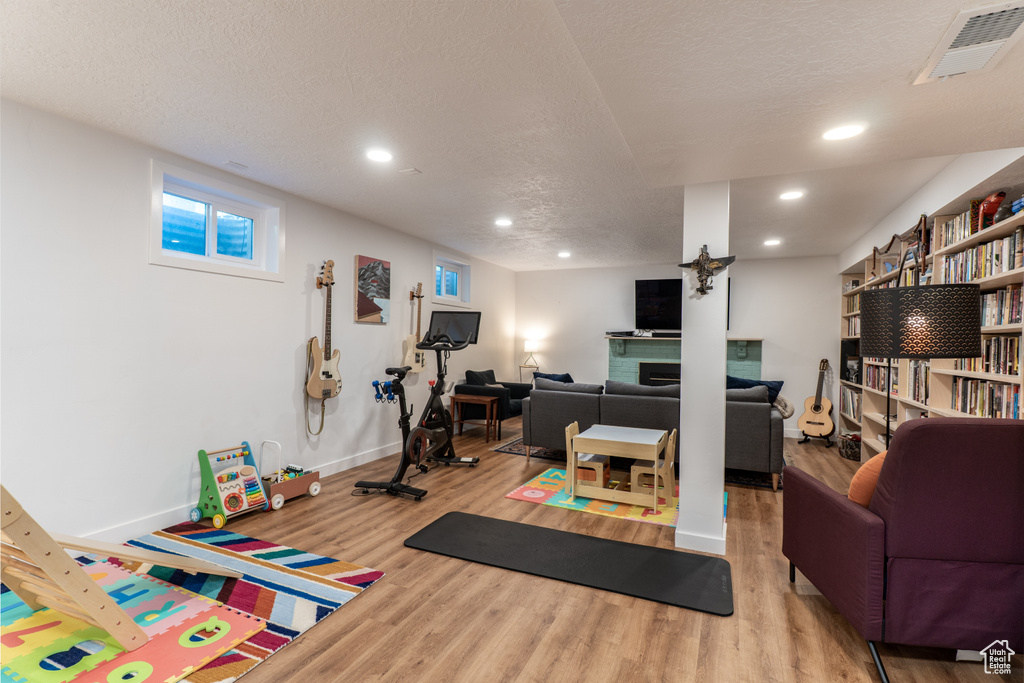 Exercise area featuring wood finished floors, baseboards, recessed lighting, a textured ceiling, and a fireplace