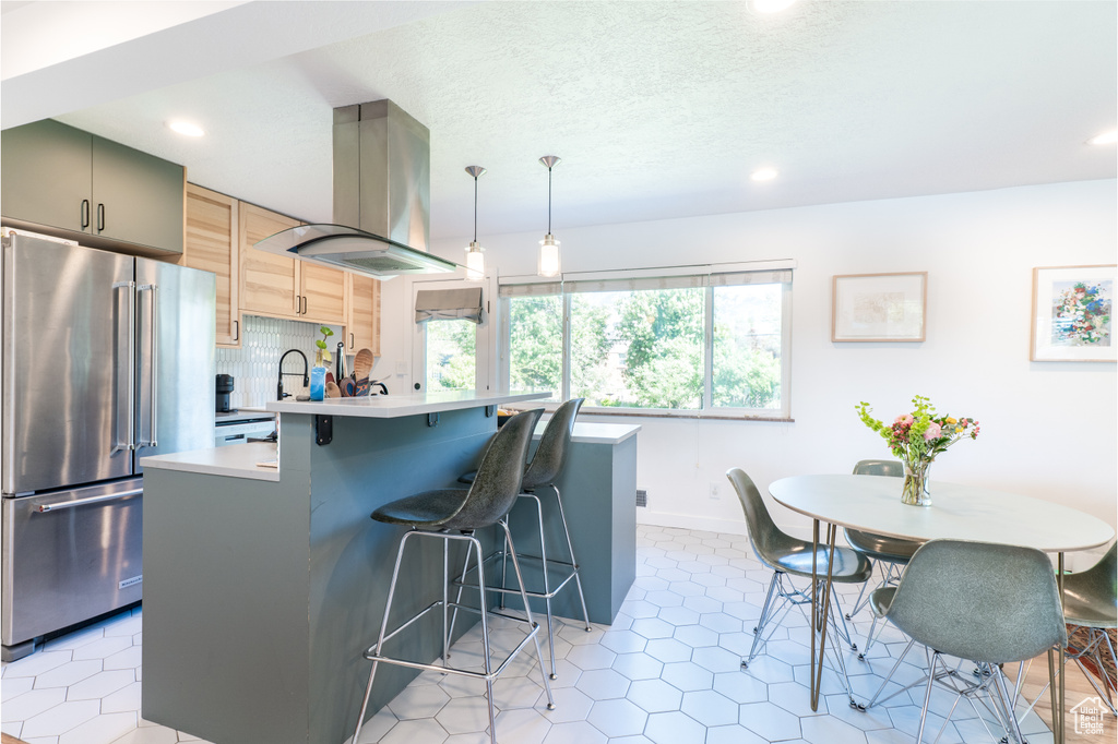 Kitchen featuring high end refrigerator, island exhaust hood, a kitchen breakfast bar, recessed lighting, and light countertops