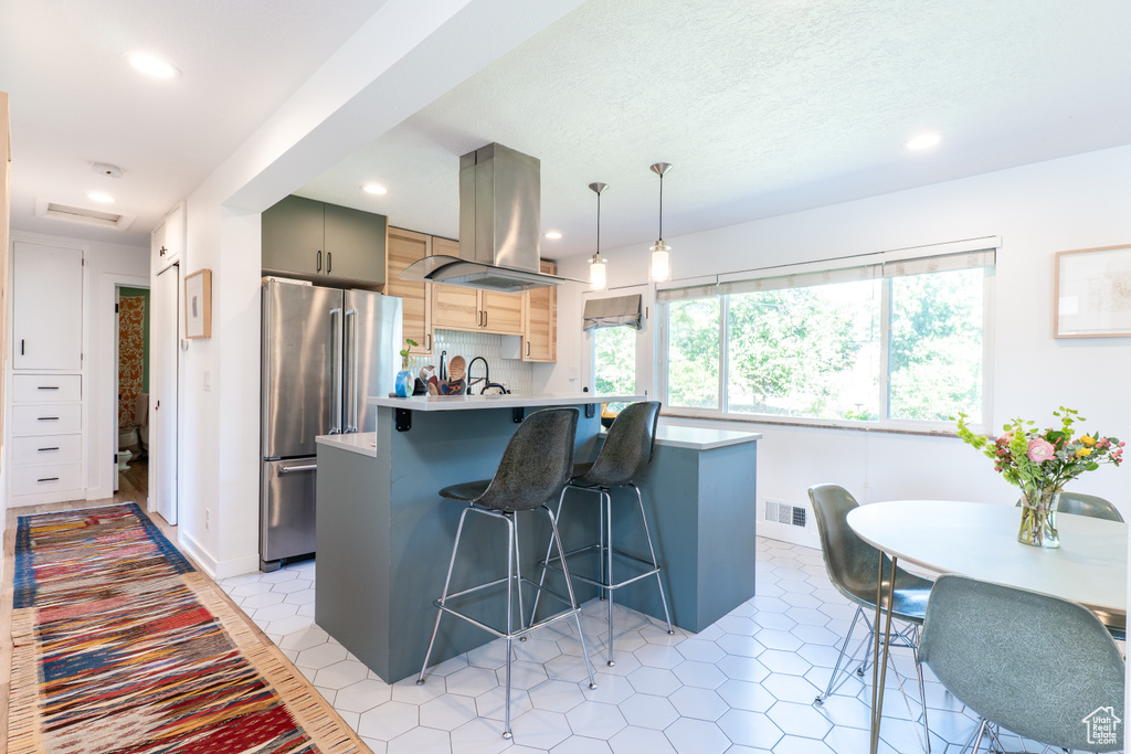 Kitchen with high end refrigerator, island exhaust hood, a breakfast bar area, recessed lighting, and light countertops