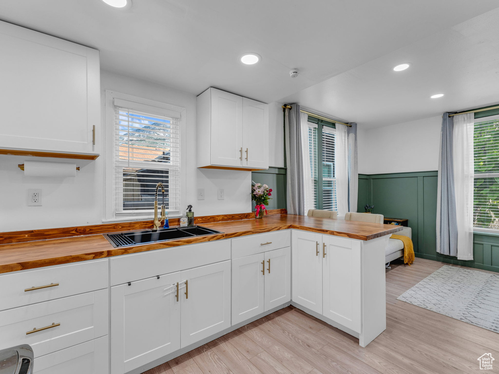 Kitchen with wood counters, a sink, a peninsula, light wood finished floors, and white cabinetry