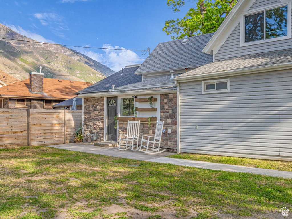 Rear view of property featuring a patio, a mountain view, stone siding, and a shingled roof