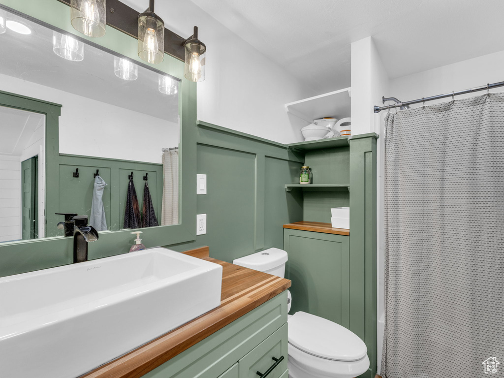 Full bathroom featuring a decorative wall, toilet, vanity, a shower with curtain, and a wainscoted wall