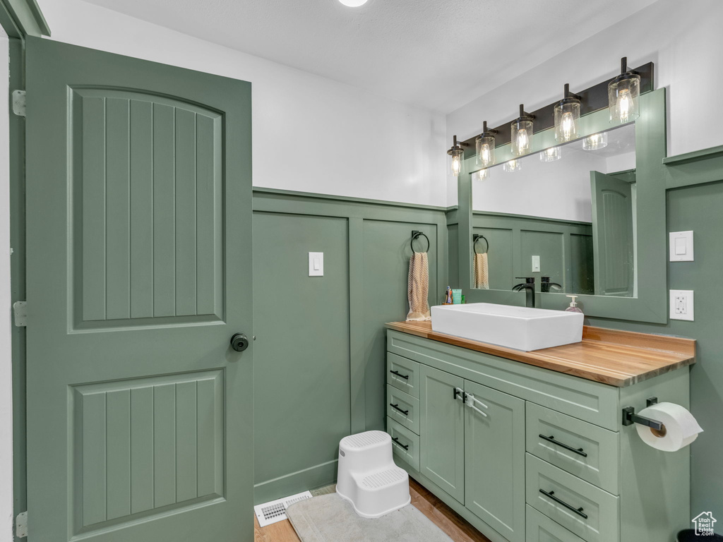 Bathroom featuring wainscoting, a decorative wall, vanity, and wood finished floors