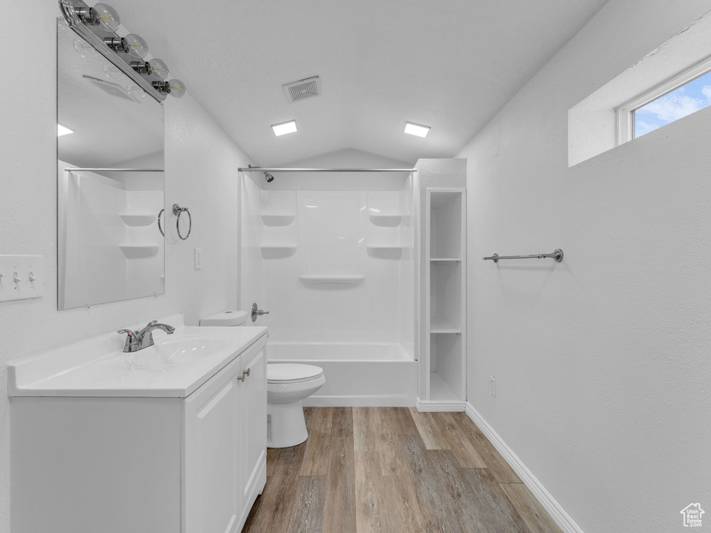 Bathroom with toilet, vanity, vaulted ceiling, wood finished floors, and bathing tub / shower combination