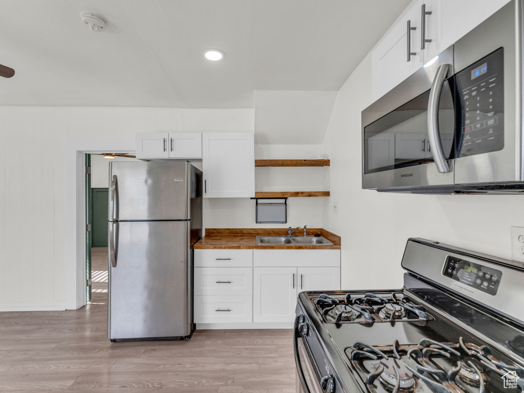 Kitchen featuring appliances with stainless steel finishes, a sink, white cabinetry, light wood finished floors, and recessed lighting