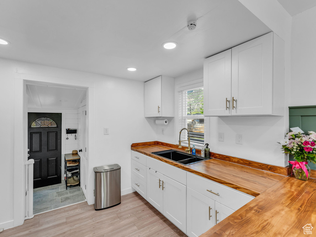 Kitchen with wooden counters, a sink, light wood finished floors, recessed lighting, and white cabinetry