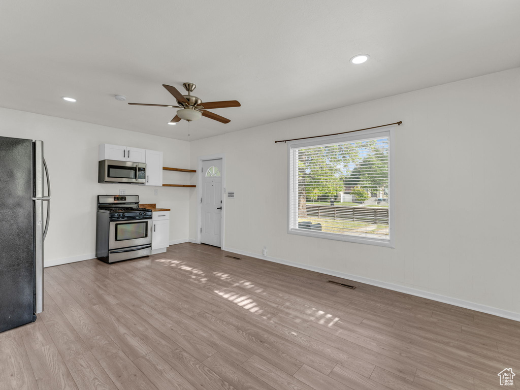 Kitchen with stainless steel appliances, ceiling fan, white cabinets, light wood-type flooring, and baseboards