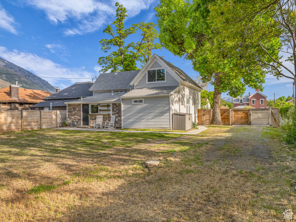 Rear view of property with a gate, a patio area, a shingled roof, central AC unit, and stone siding