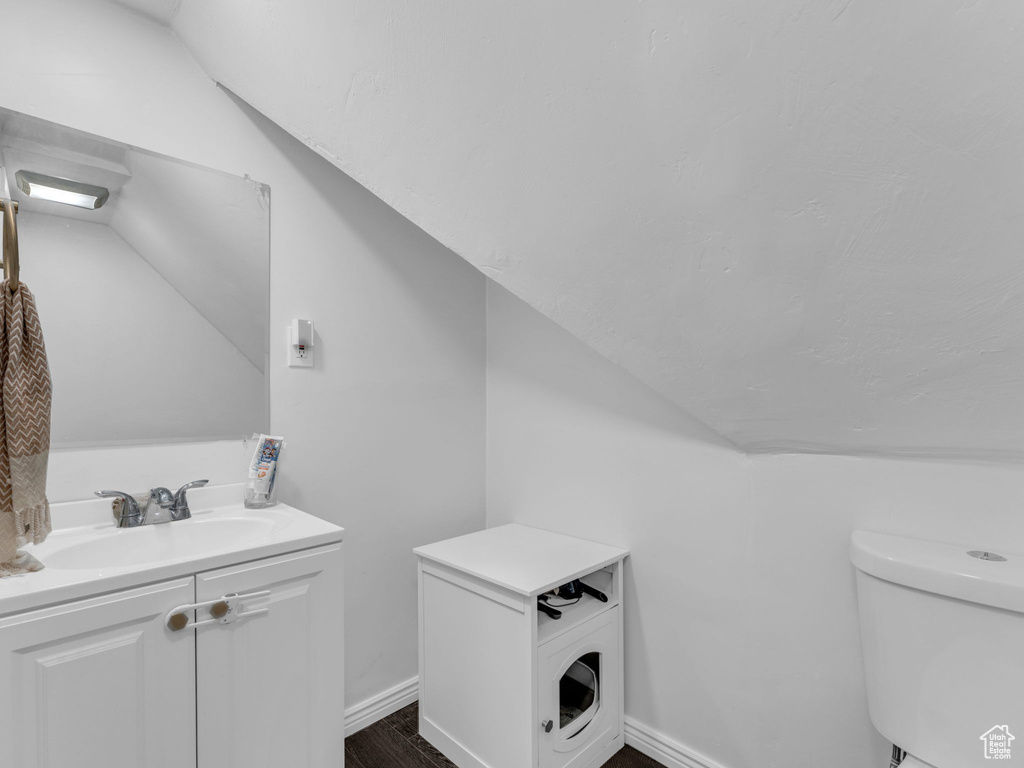 Bathroom with vaulted ceiling, toilet, vanity, baseboards, and wood finished floors