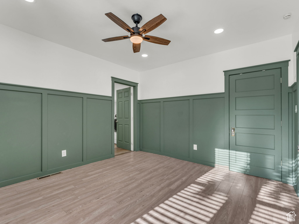 Unfurnished bedroom with a decorative wall, light wood finished floors, wainscoting, recessed lighting, and a ceiling fan