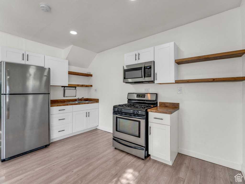 Kitchen with open shelves, appliances with stainless steel finishes, baseboards, a sink, and light wood-type flooring