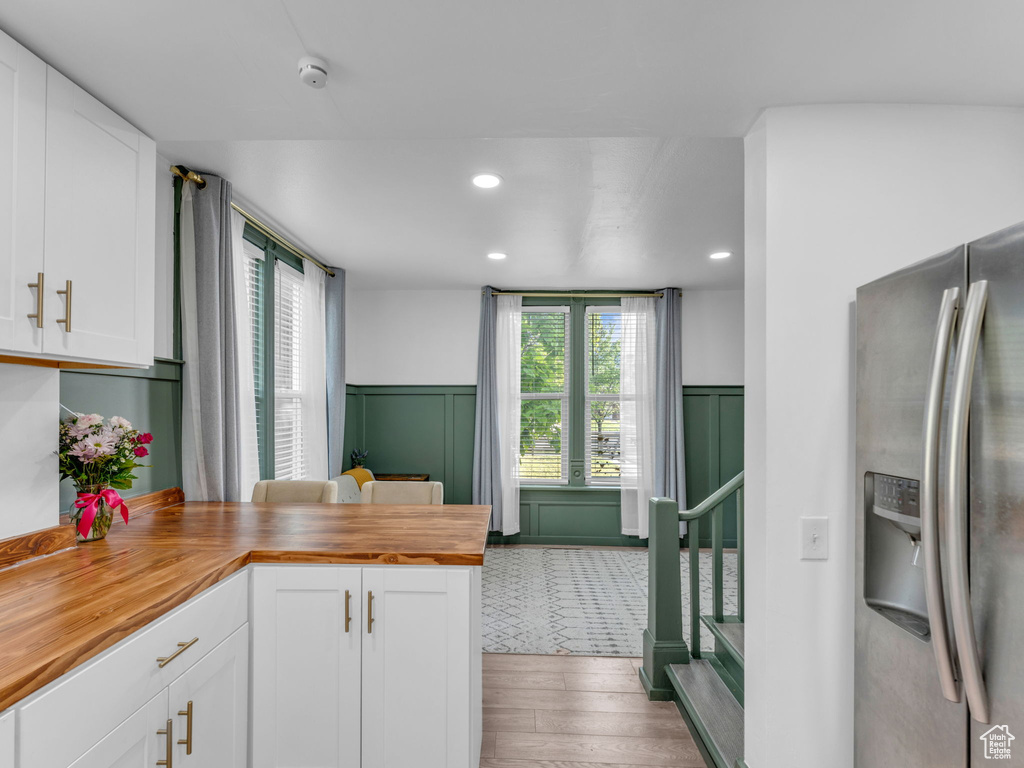 Kitchen with stainless steel fridge with ice dispenser, wooden counters, wood finished floors, white cabinets, and a wainscoted wall
