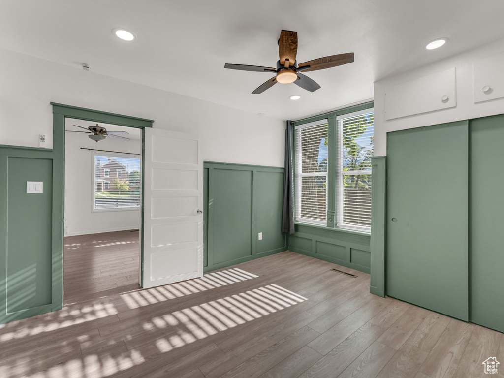 Unfurnished bedroom featuring a decorative wall, light wood-style floors, multiple windows, a wainscoted wall, and recessed lighting
