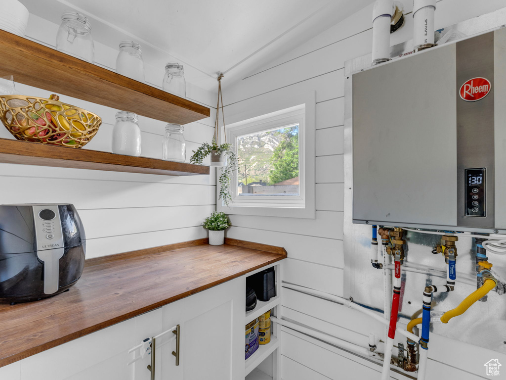 Kitchen with wooden counters, open shelves, water heater, white cabinets, and vaulted ceiling