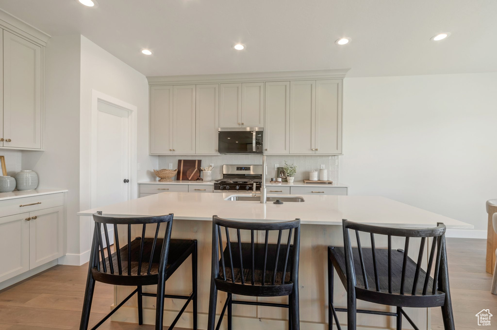 Kitchen with appliances with stainless steel finishes, light wood finished floors, light countertops, a breakfast bar, and recessed lighting