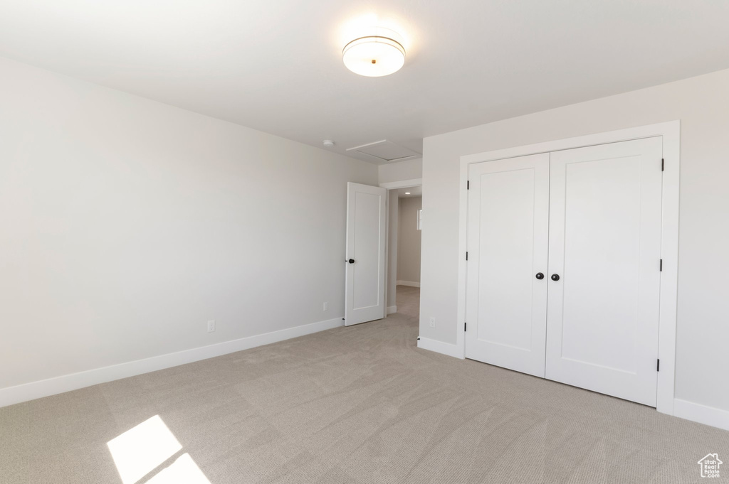 Unfurnished bedroom with light colored carpet, baseboards, a closet, and attic access