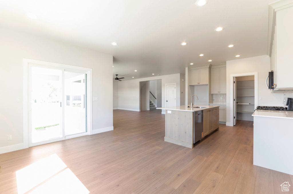 Kitchen featuring appliances with stainless steel finishes, open floor plan, a sink, light wood-style flooring, and a center island with sink