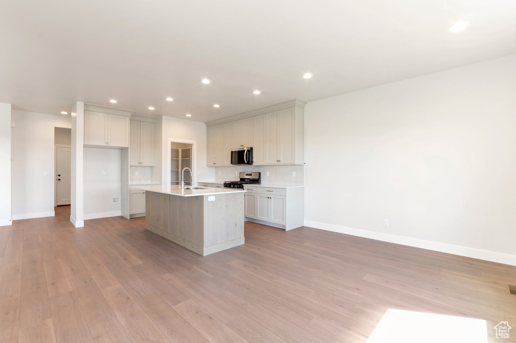 Kitchen with appliances with stainless steel finishes, light wood finished floors, a kitchen island with sink, baseboards, and light countertops