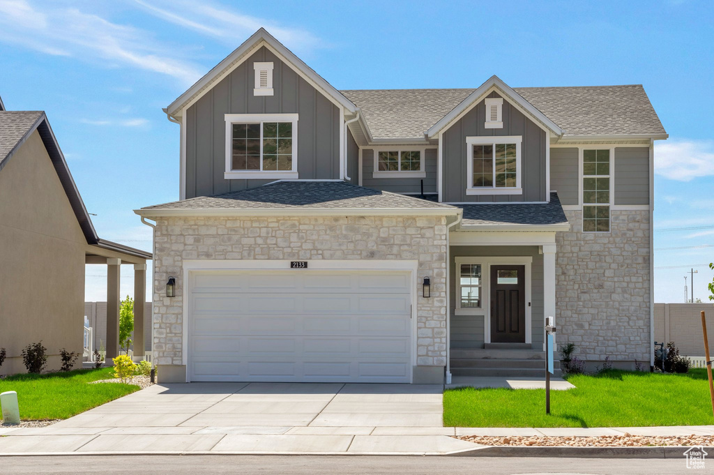 View of front of home with stone siding, board and batten siding, driveway, and a shingled roof