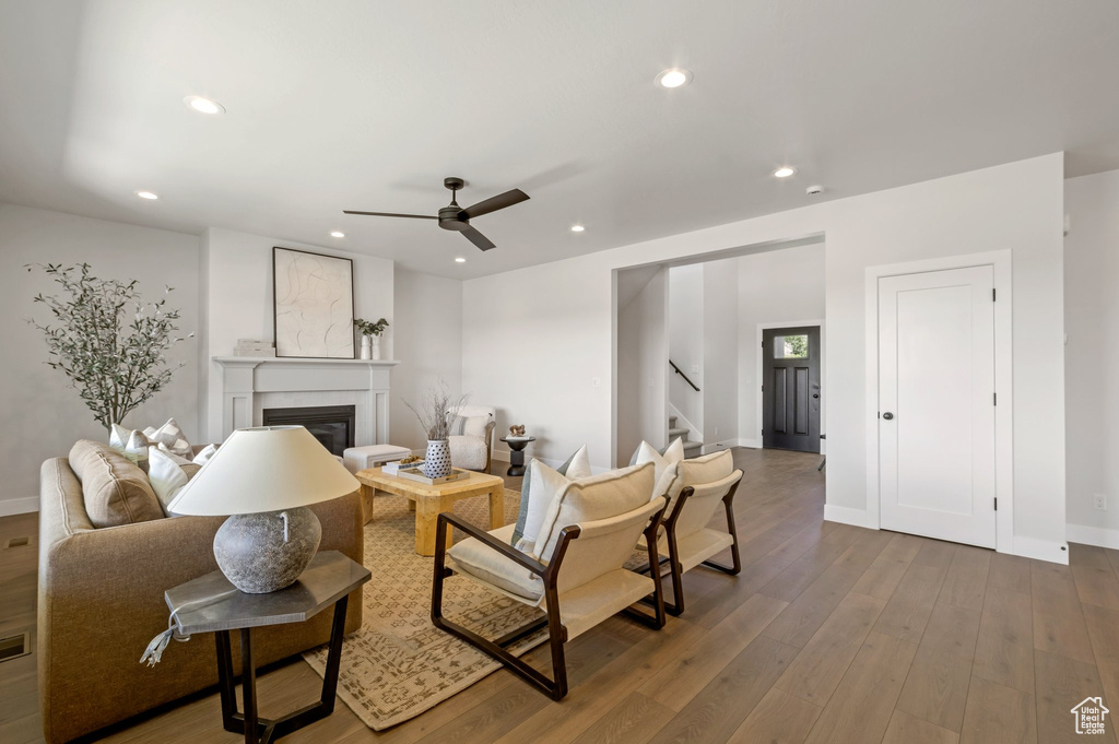 Living room featuring stairs, a glass covered fireplace, ceiling fan, wood finished floors, and recessed lighting