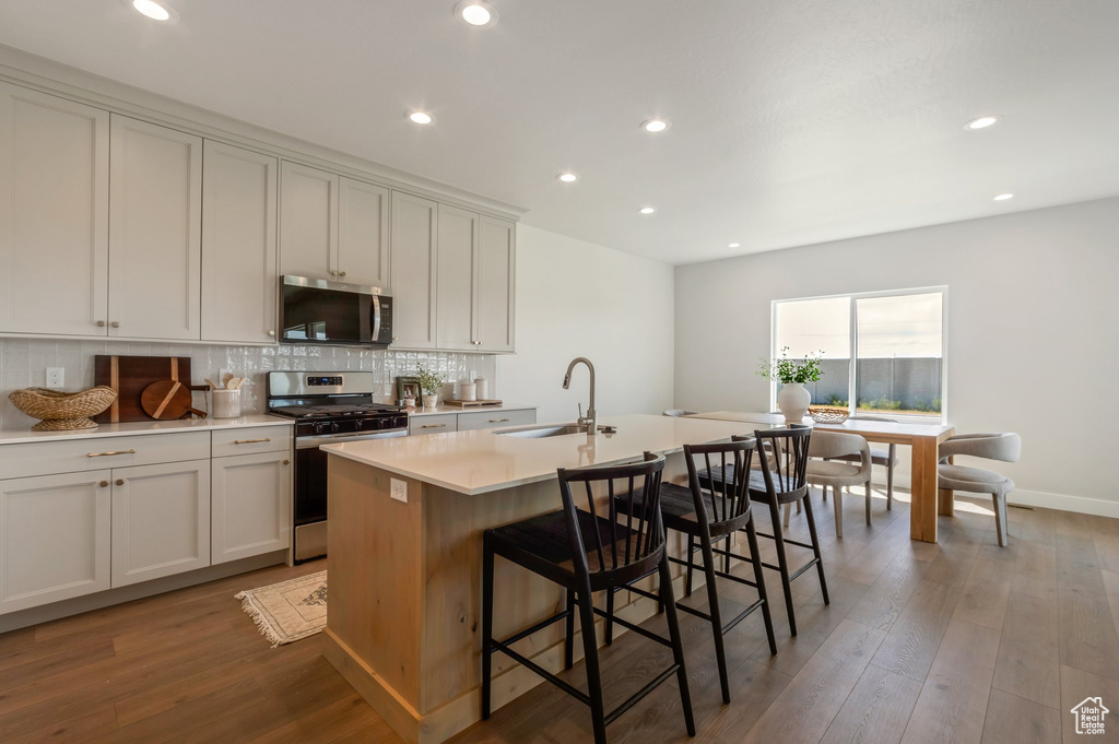 Kitchen featuring appliances with stainless steel finishes, backsplash, an island with sink, wood finished floors, and recessed lighting