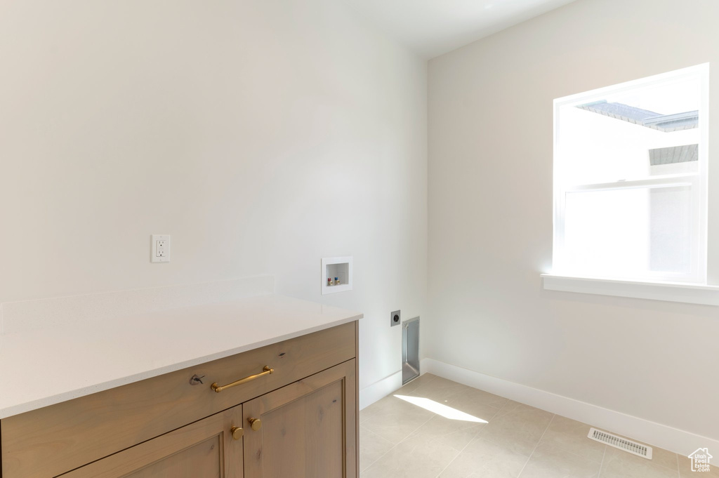 Laundry room with hookup for an electric dryer, hookup for a washing machine, cabinet space, baseboards, and light tile patterned flooring