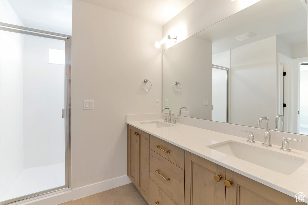 Bathroom featuring a shower stall, tile patterned floors, double vanity, and baseboards