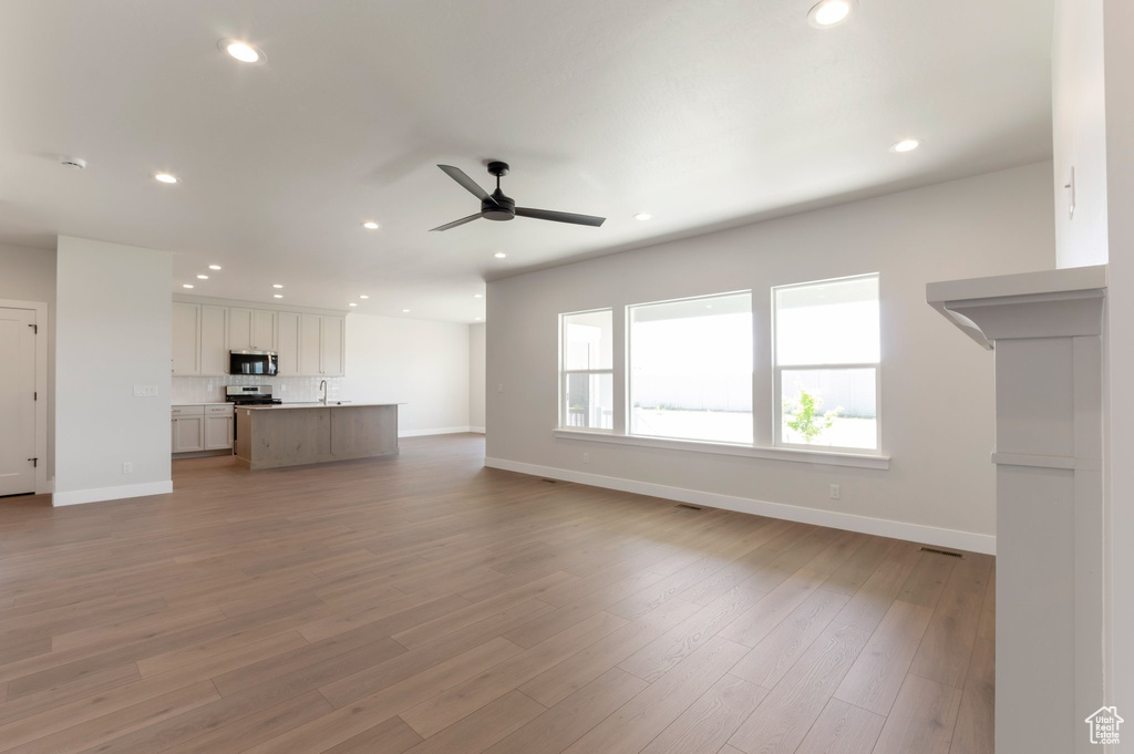 Unfurnished living room with a ceiling fan, recessed lighting, baseboards, light wood-style floors, and a sink