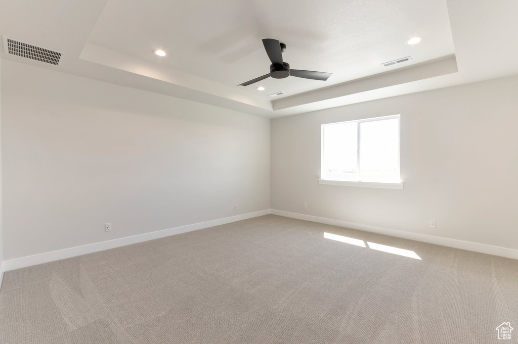 Empty room with a tray ceiling, a ceiling fan, recessed lighting, baseboards, and light colored carpet
