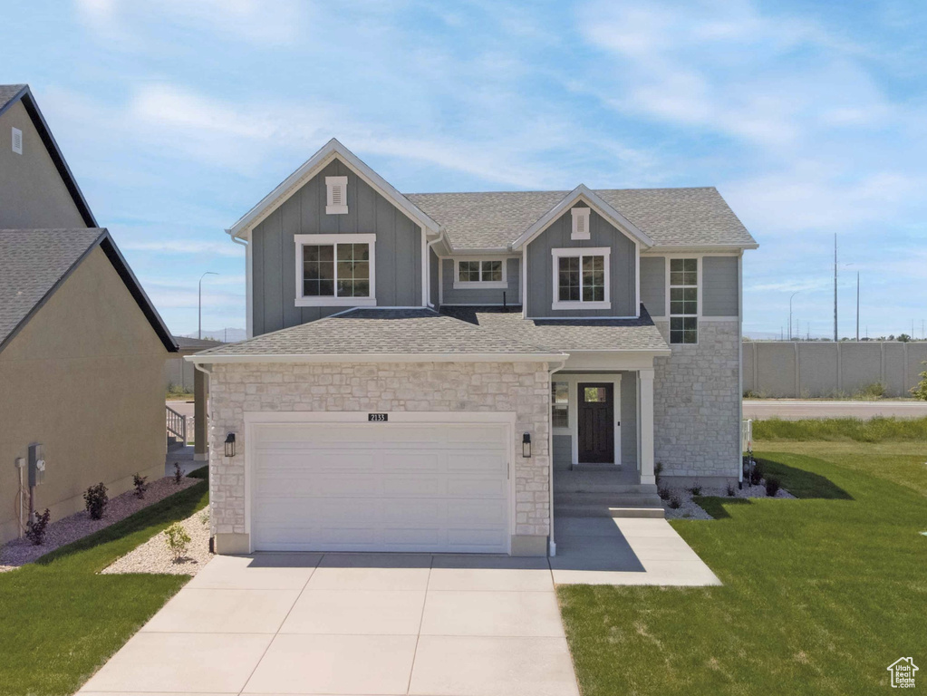 View of front of property with stone siding, concrete driveway, board and batten siding, and a shingled roof