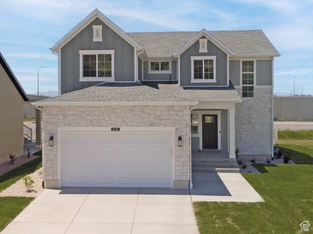 View of front of property with stone siding, concrete driveway, board and batten siding, and a shingled roof
