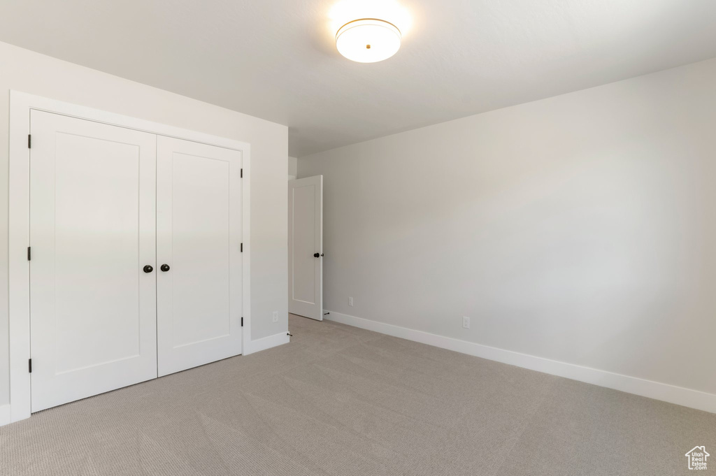 Unfurnished bedroom featuring light colored carpet, baseboards, and a closet