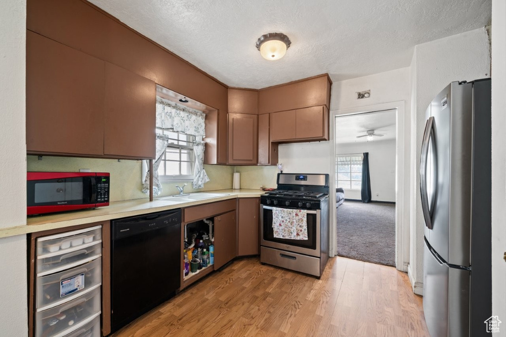 Kitchen featuring appliances with stainless steel finishes, a sink, light countertops, a textured ceiling, and light wood-style flooring