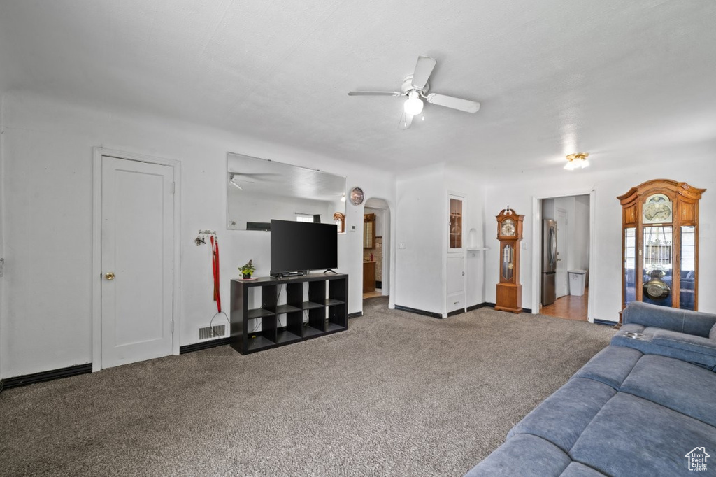 Living room with ceiling fan, carpet, baseboards, and arched walkways