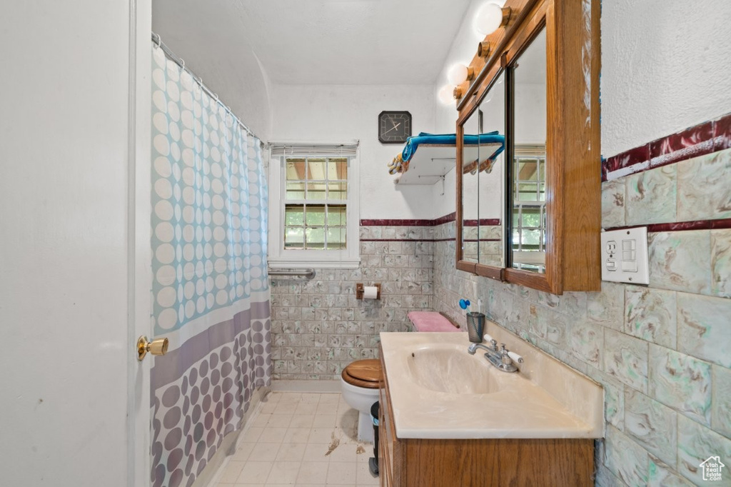 Full bathroom featuring toilet, vanity, tile patterned flooring, wainscoting, and curtained shower