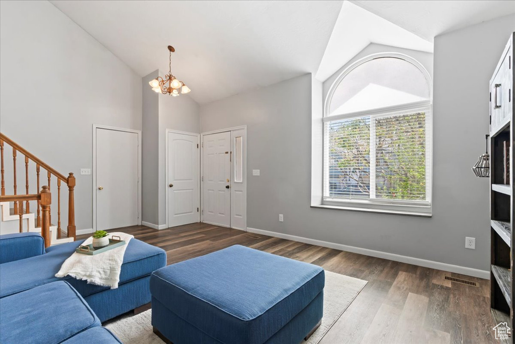 Living area with wood finished floors, a chandelier, stairs, high vaulted ceiling, and baseboards