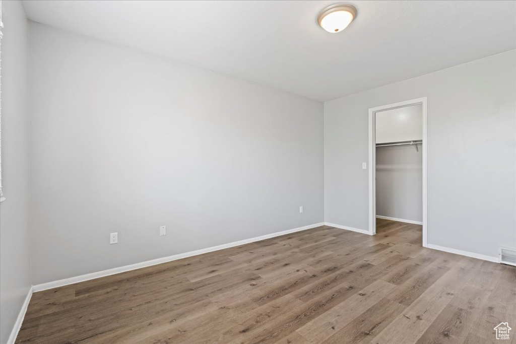 Unfurnished bedroom featuring wood finished floors, baseboards, a spacious closet, and a closet