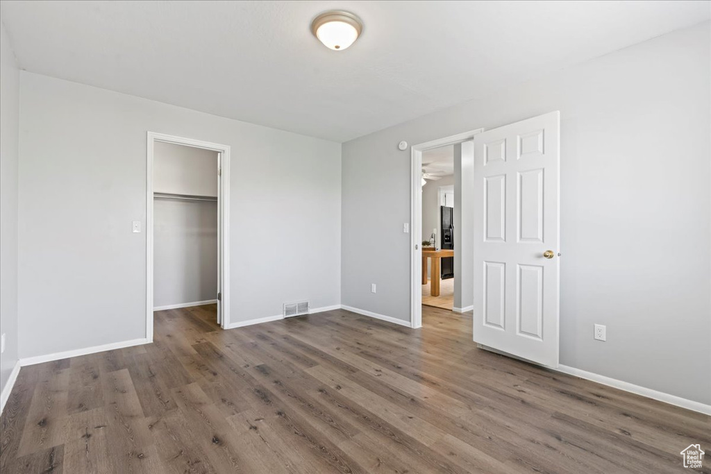 Unfurnished bedroom featuring wood finished floors, baseboards, and a walk in closet